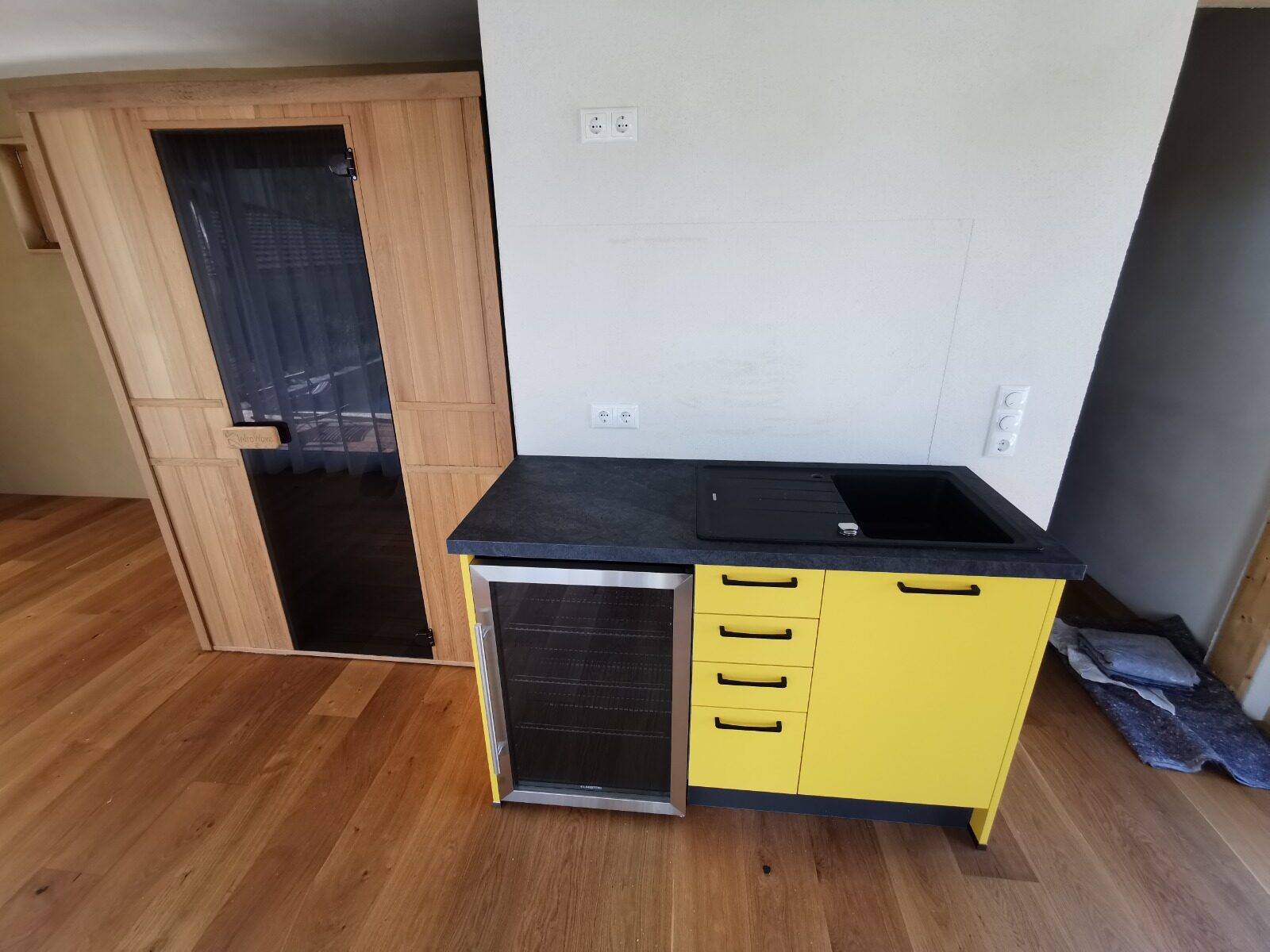 Gelbe Kompaktküche mit dunkler Arbeitsplatte neben einer Sauna