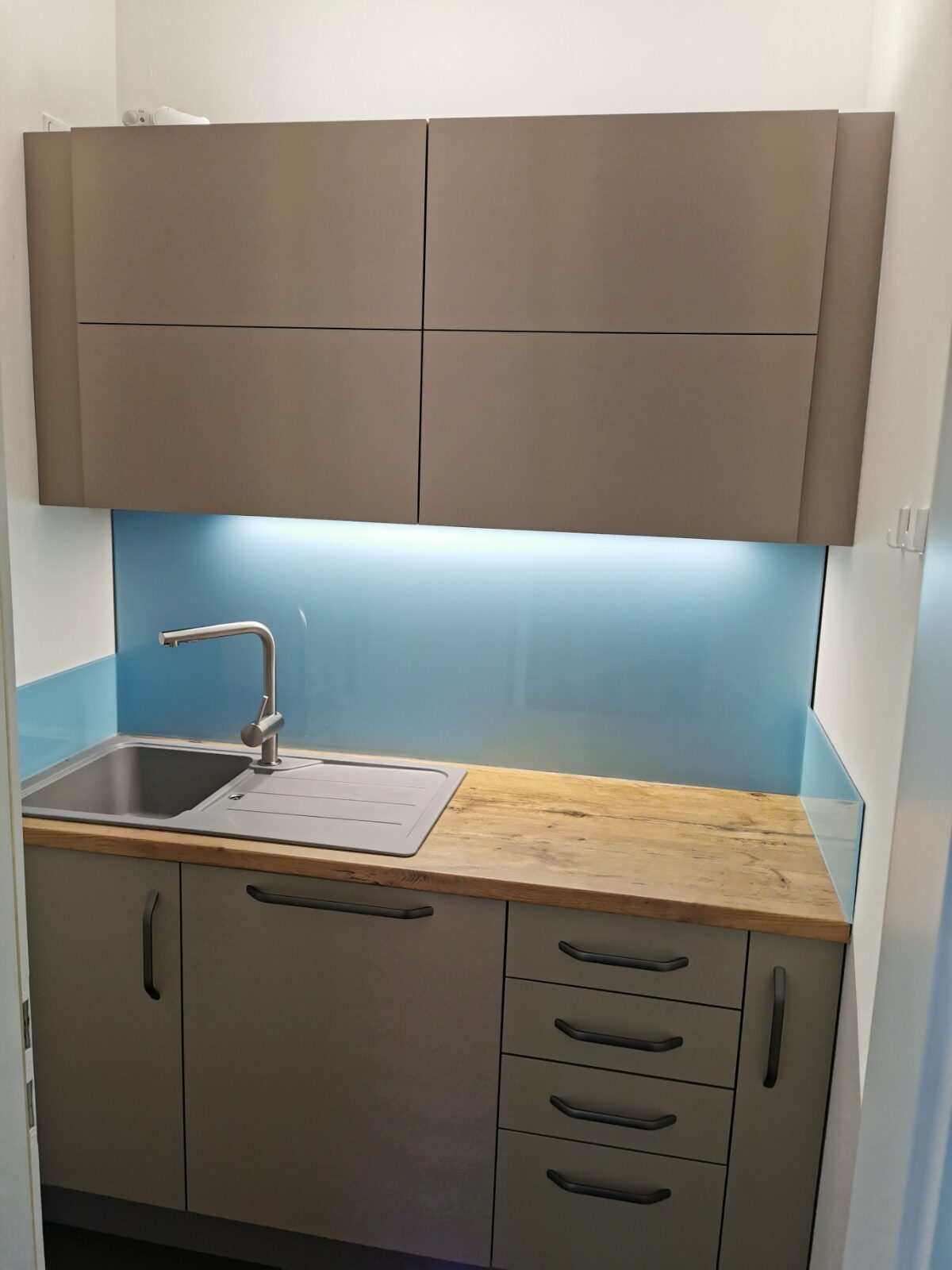 Kompaktküche mit blauer Glasrückwand und Holz-Arbeitsplatte